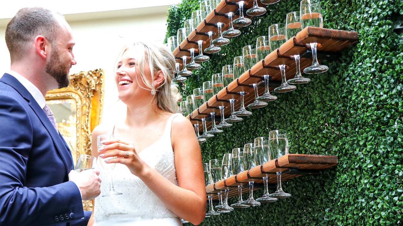 Guests enjoying wine by a lush green wall with elegant glass display, perfect for celebrations at this charming hotel.