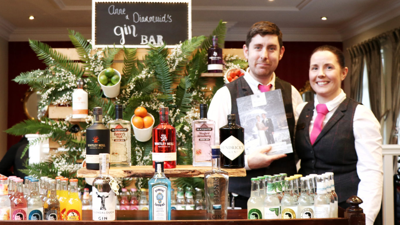 Friendly staff at an elegant gin bar with vibrant drink selection, lush greenery, and inviting atmosphere for guests.