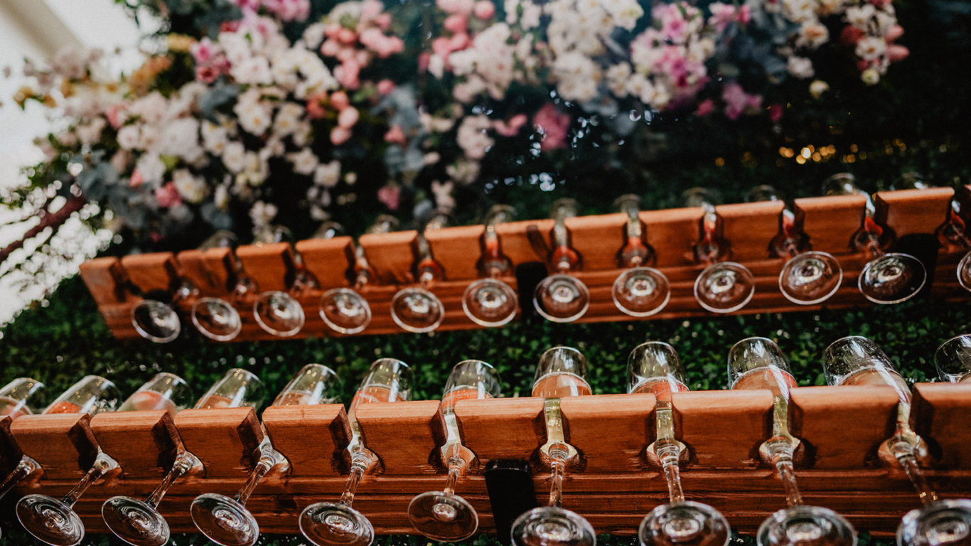 Elegant wine glasses hang on a stylish wall rack with lush floral decor, creating a luxurious hotel ambiance.
