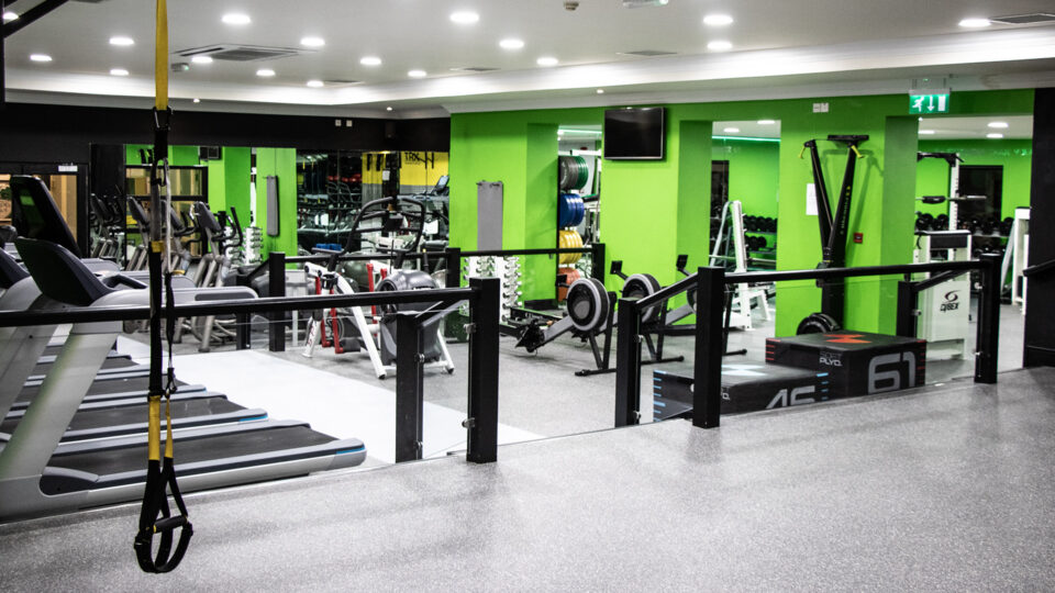 Modern gym with bright green walls, treadmills, weights, and rowing machines, offering a dynamic workout experience.