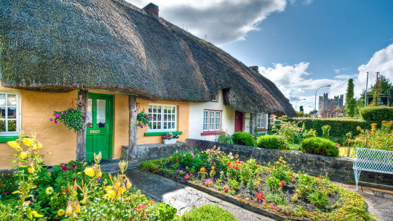 Charming cottage with a thatched roof, vibrant garden blooms, and a welcoming green door in a picturesque countryside.