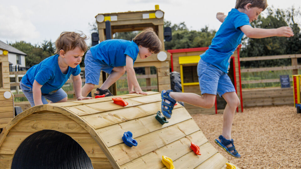 Children enjoying wooden play area at family-friendly hotel with climbing equipment and safety flooring.