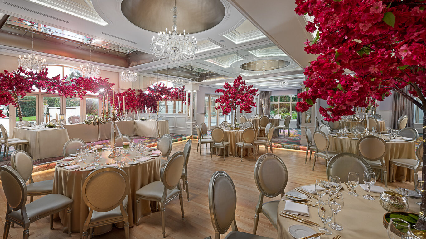 Elegant ballroom with chandeliers, floral decor, round tables set for dining, and large windows, perfect for events.