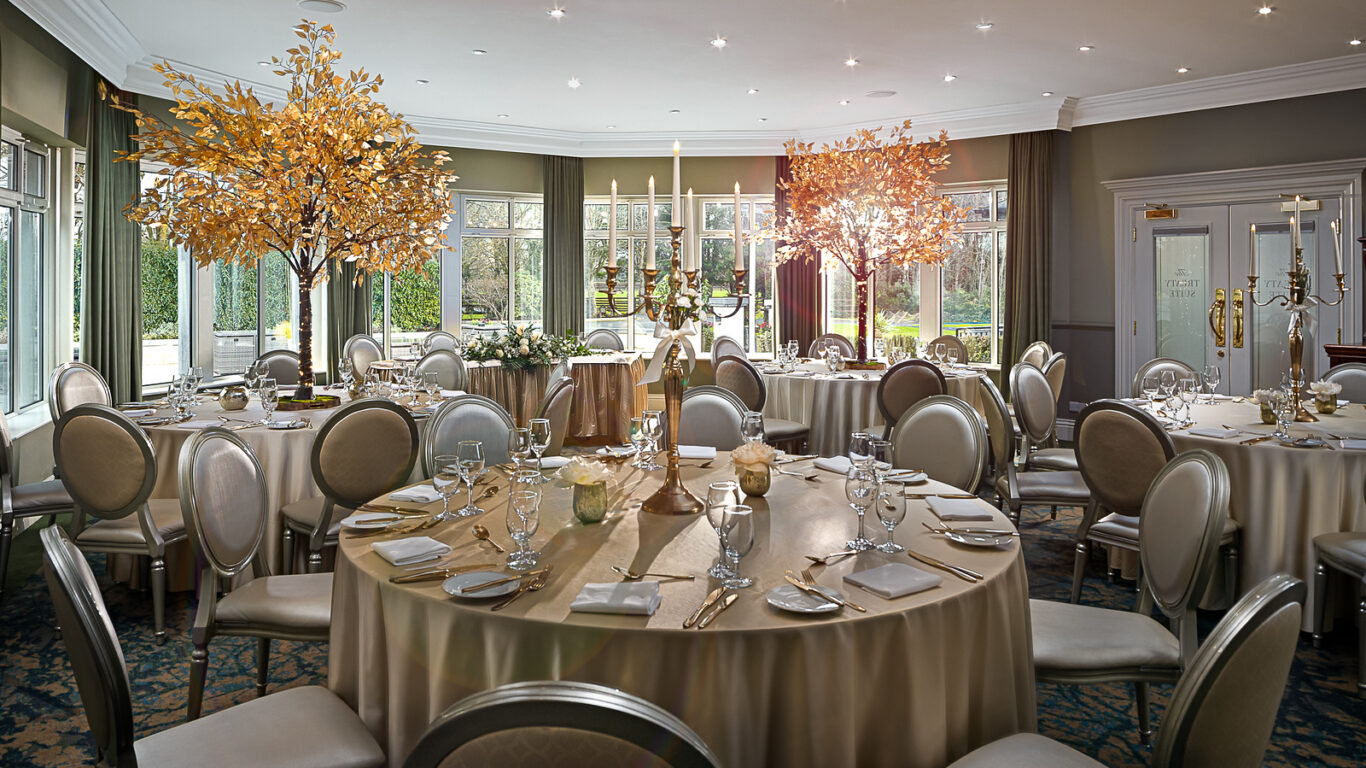 Elegant banquet room with round tables, lush decor, and ambient lighting, perfect for weddings or events.