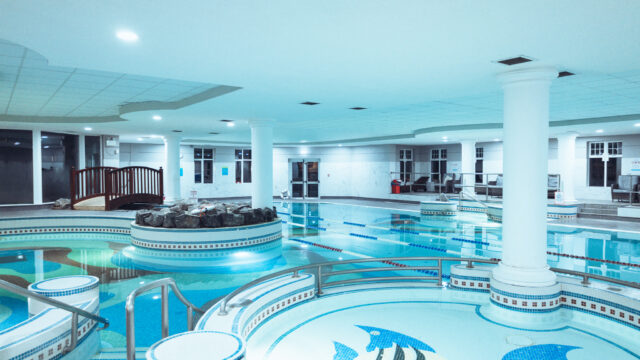 Spacious indoor pool with mosaic fish design, elegant columns, wooden bridge, and comfortable loungers for relaxation.