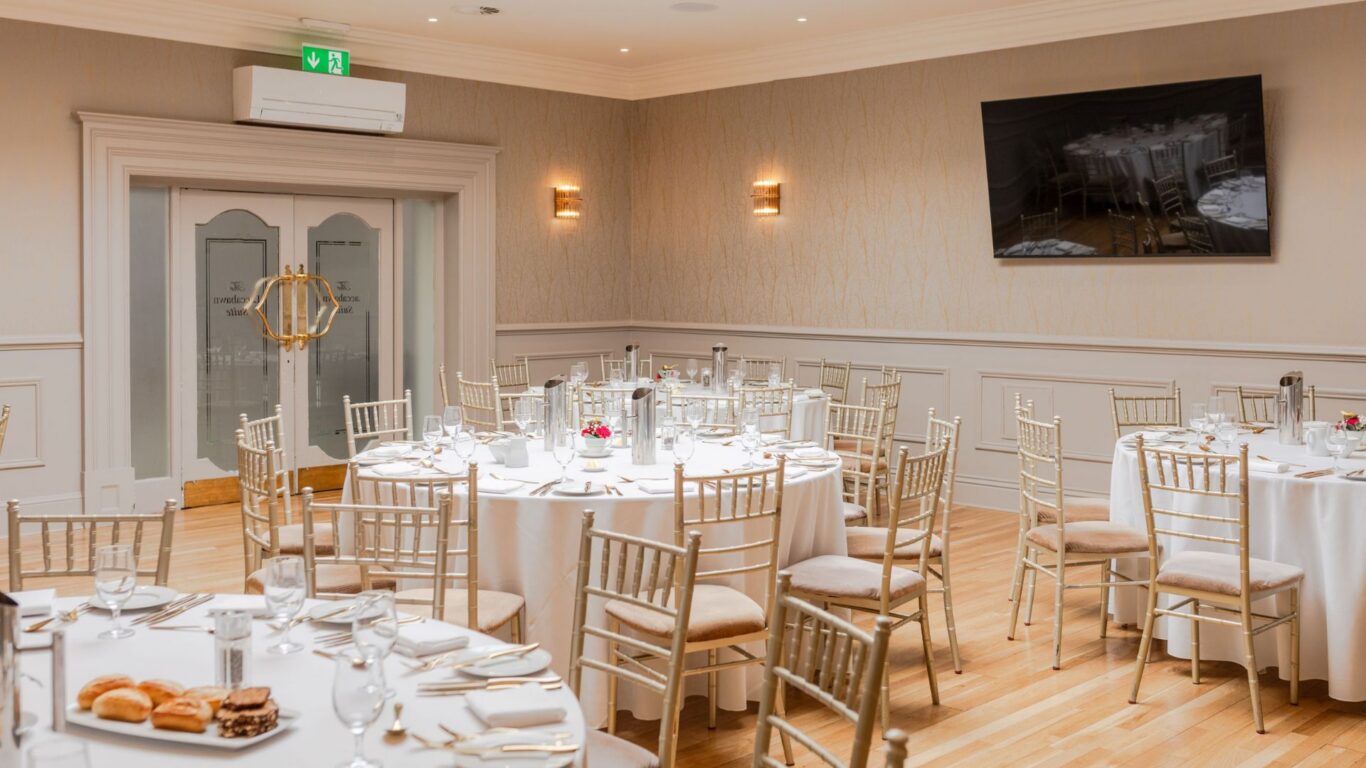 Elegant hotel banquet room with round tables, white linens, and stylish chairs set for dining. Perfect for events and receptions.