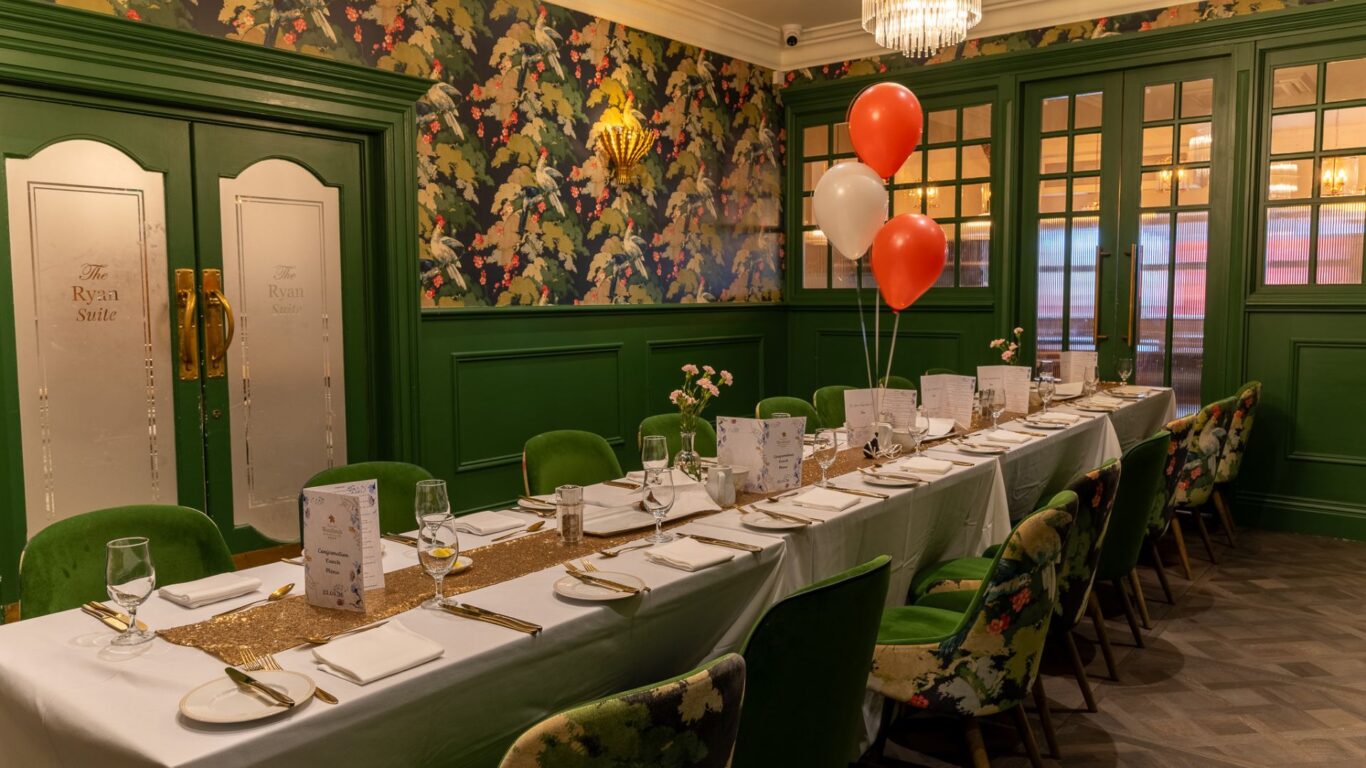 Elegant private dining room with floral chairs, festive balloons, and a long table set for an exquisite dining experience.