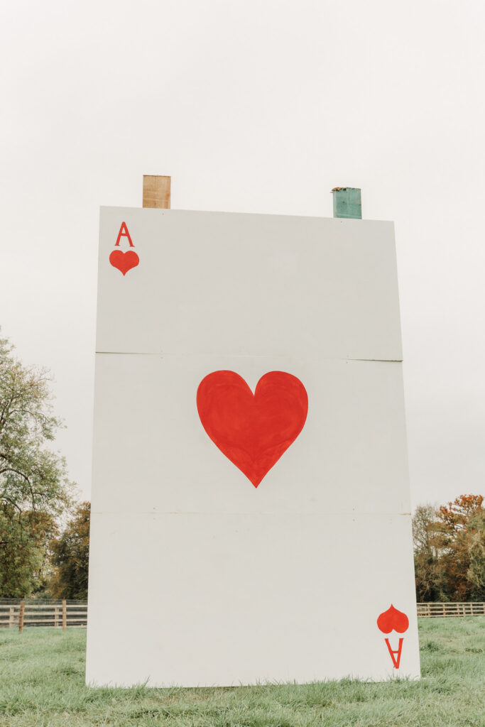 Giant Ace of Hearts card sculpture in lush garden setting, perfect for unique outdoor events and picturesque photo spots.