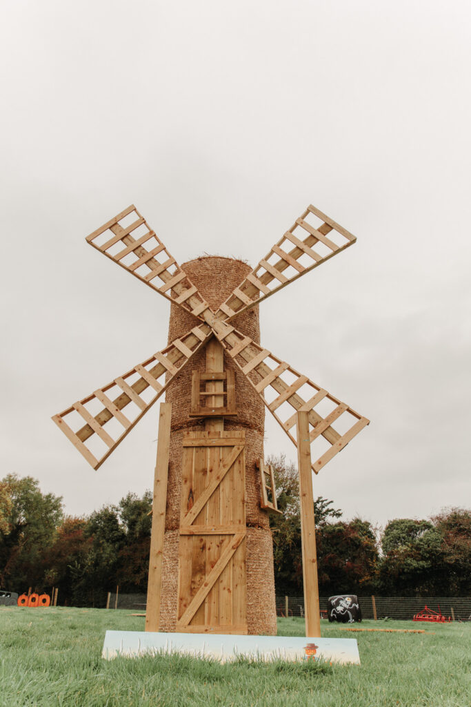Rustic wooden windmill in lush garden, perfect for relaxing walks, adding charm to hotel stay. Enjoy serene natural views.