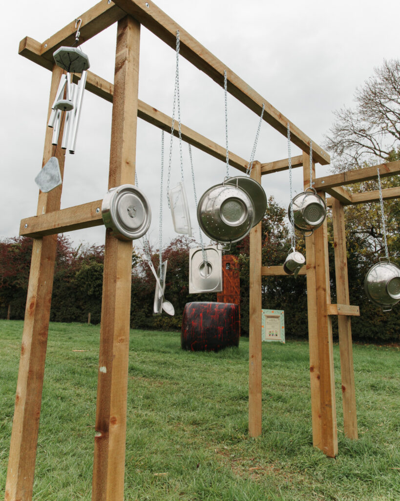 Family-friendly music play area with hanging metal utensils on wooden frames in lush garden setting.