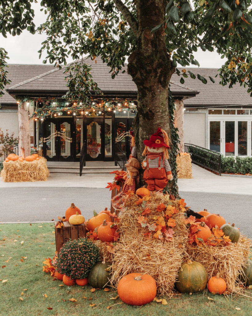 Cosy hotel entrance adorned with autumn pumpkins, hay bales, and festive lights, welcoming guests to a charming seasonal stay.