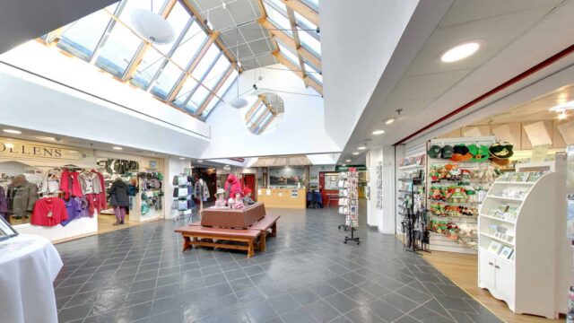 Bright hotel lobby with shops, skylight ceiling, and comfortable seating, offering clothing, gifts, and local treats.
