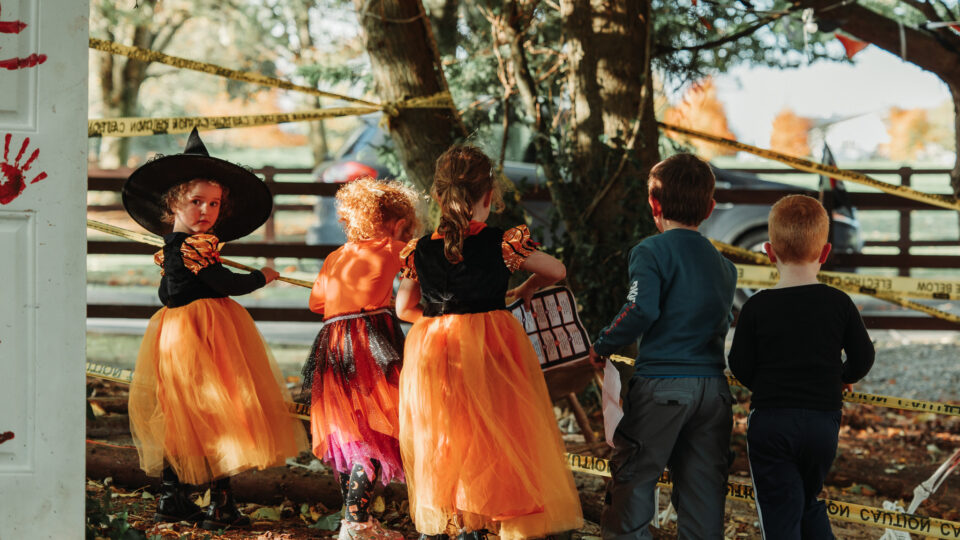 Children in festive costumes exploring a Halloween-themed garden at a family-friendly hotel, surrounded by autumn decor.