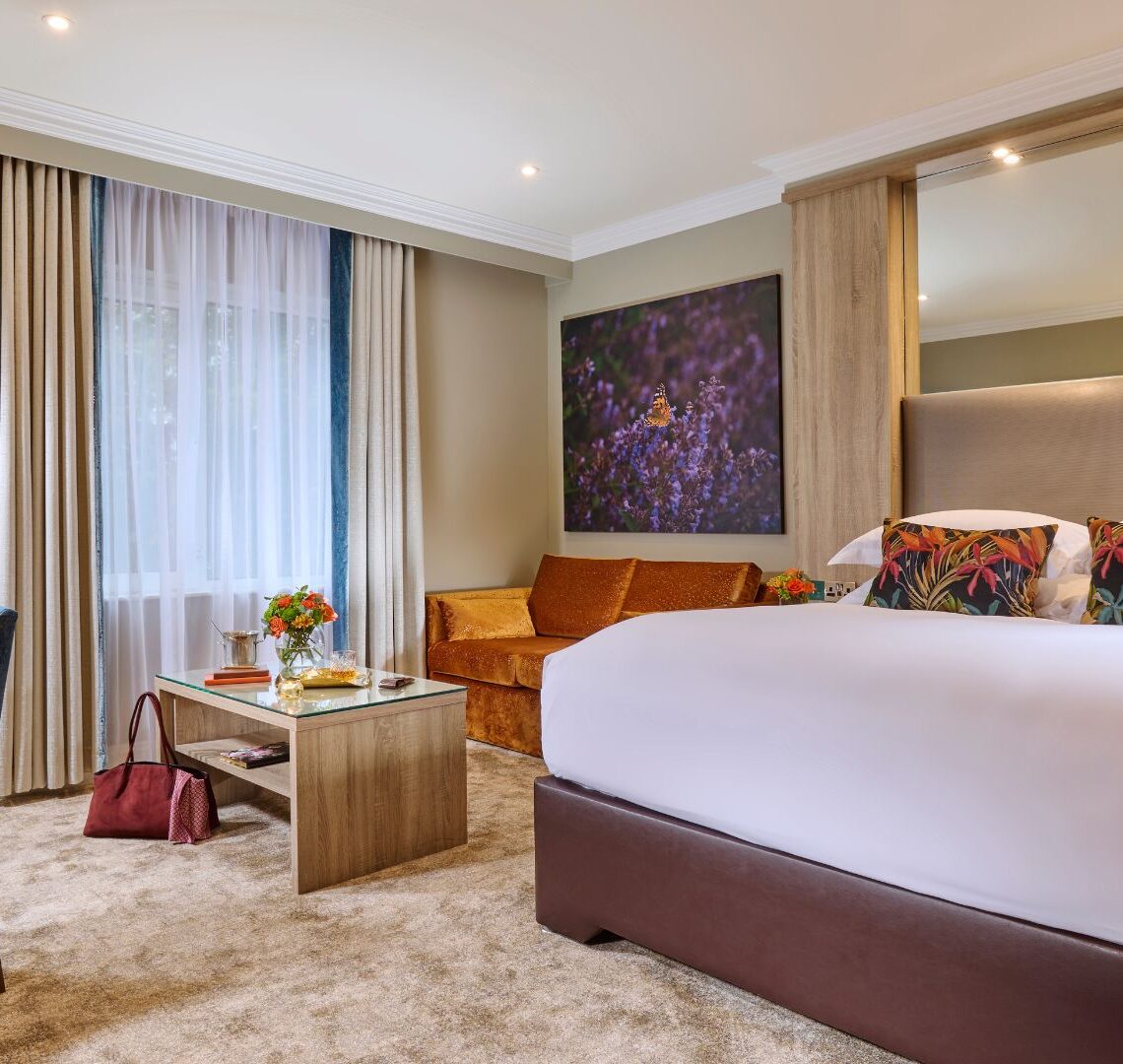 Elegant hotel room with king bed, plush cushions, cosy sofa, stylish desk, and warm lighting for ultimate relaxation.