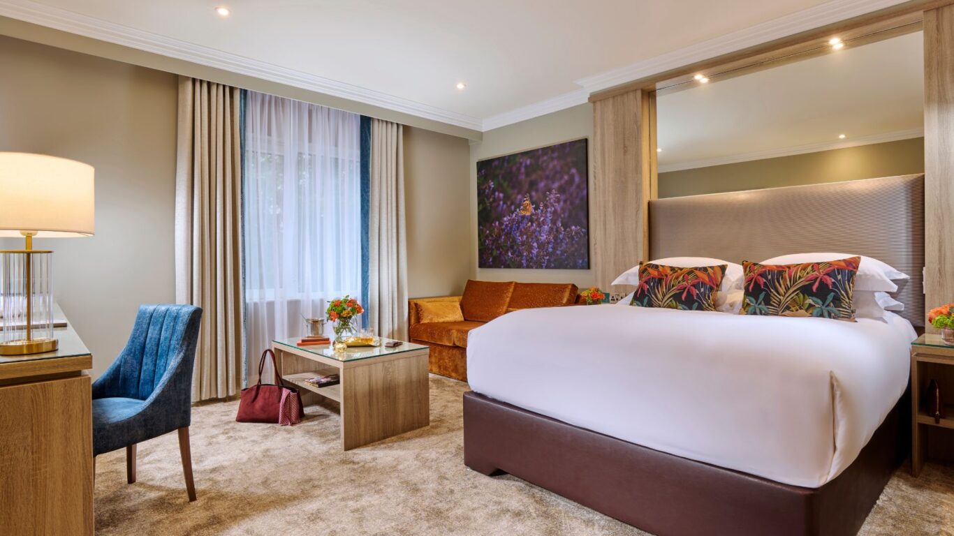 Elegant hotel room with king bed, plush cushions, cosy sofa, stylish desk, and warm lighting for ultimate relaxation.