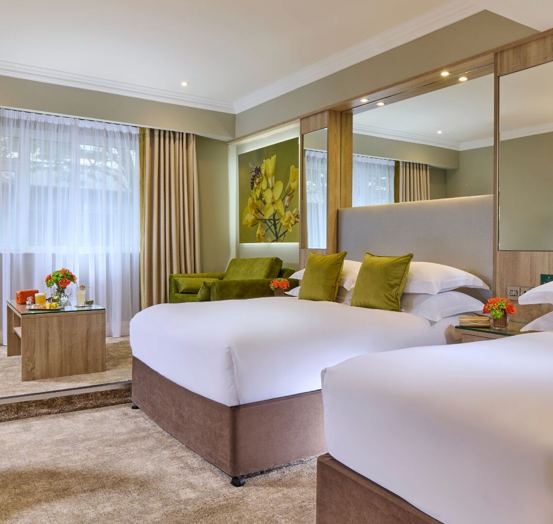Spacious hotel room with twin beds, plush pillows, stylish decor, large windows, and modern desk; perfect for relaxation.