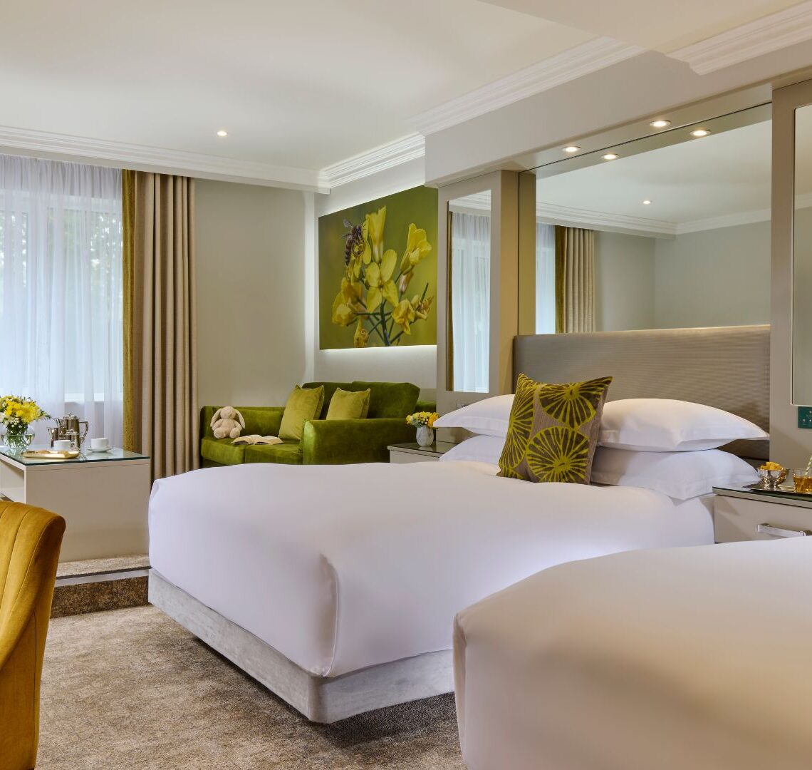 Elegant hotel room with twin beds, cosy seating, bright decor, modern amenities, and garden view.