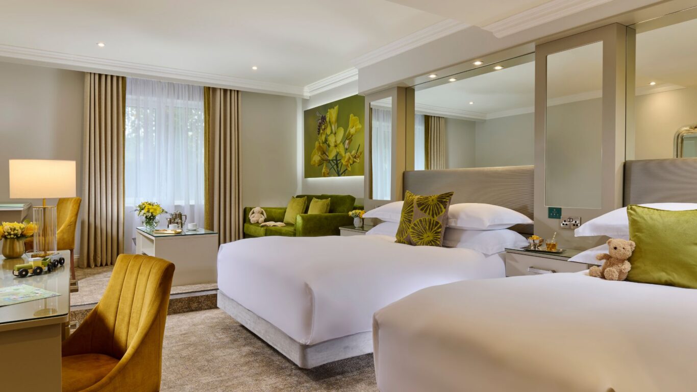 Elegant hotel room with twin beds, cosy seating, bright decor, modern amenities, and garden view.