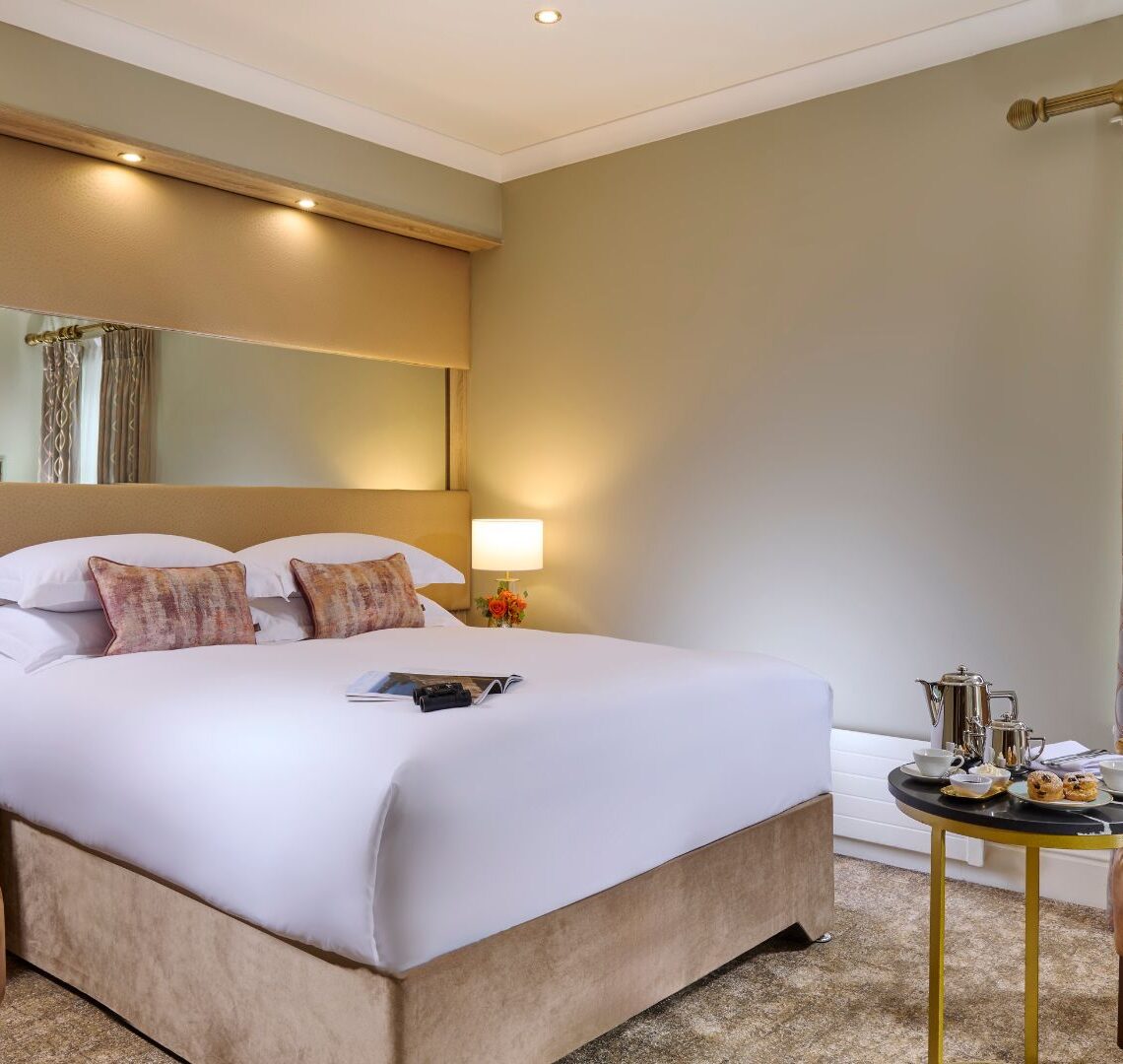 Elegant hotel room with plush bedding, armchairs, and a table set with afternoon tea, offering a cosy and relaxing atmosphere.