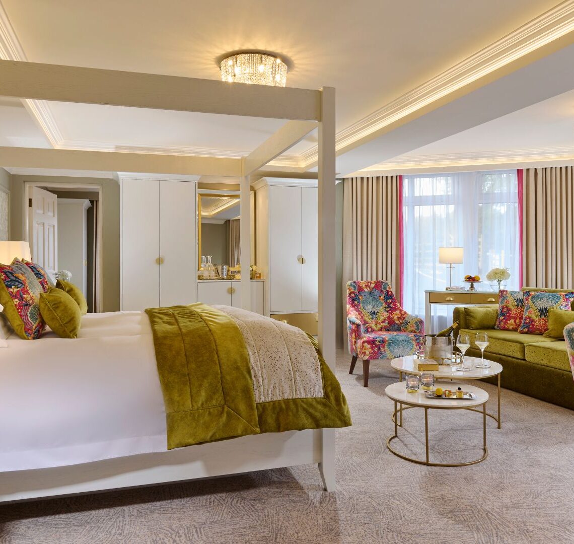 Spacious hotel suite with king canopy bed, vibrant sofa, elegant d&eacute;cor, and natural light, ideal for a relaxing stay.