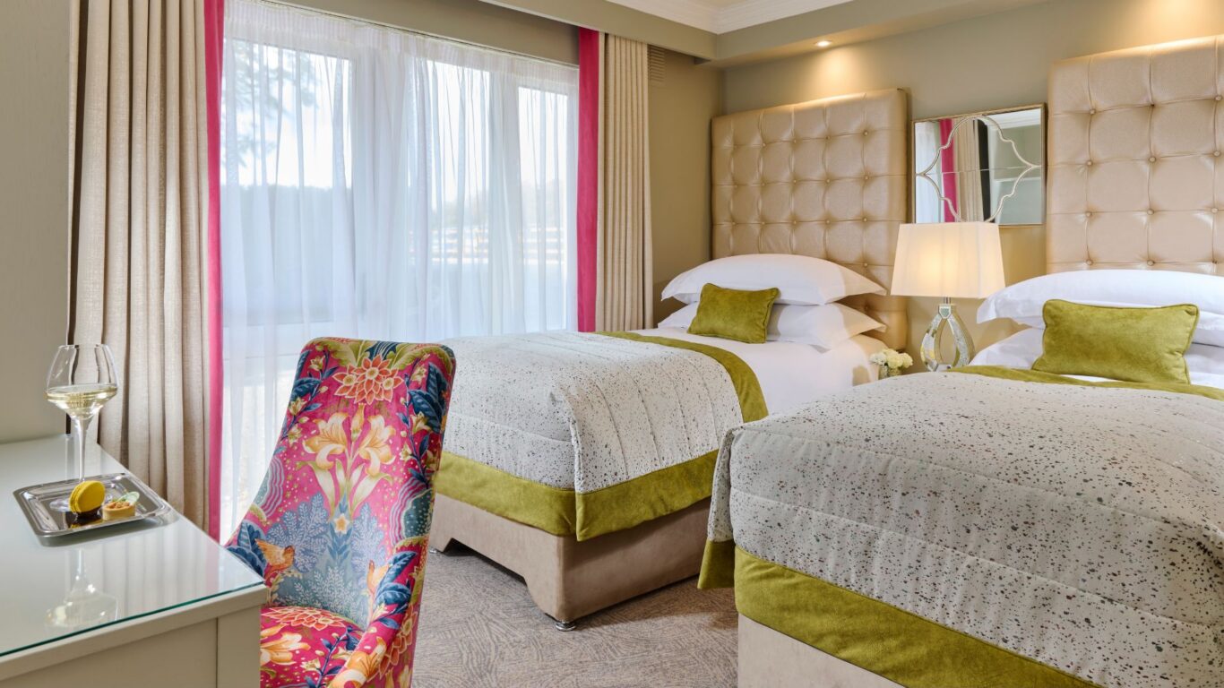 Elegant twin room with plush beds, vibrant chair, soft lighting, and a view of serene nature. Ideal for a relaxing stay.